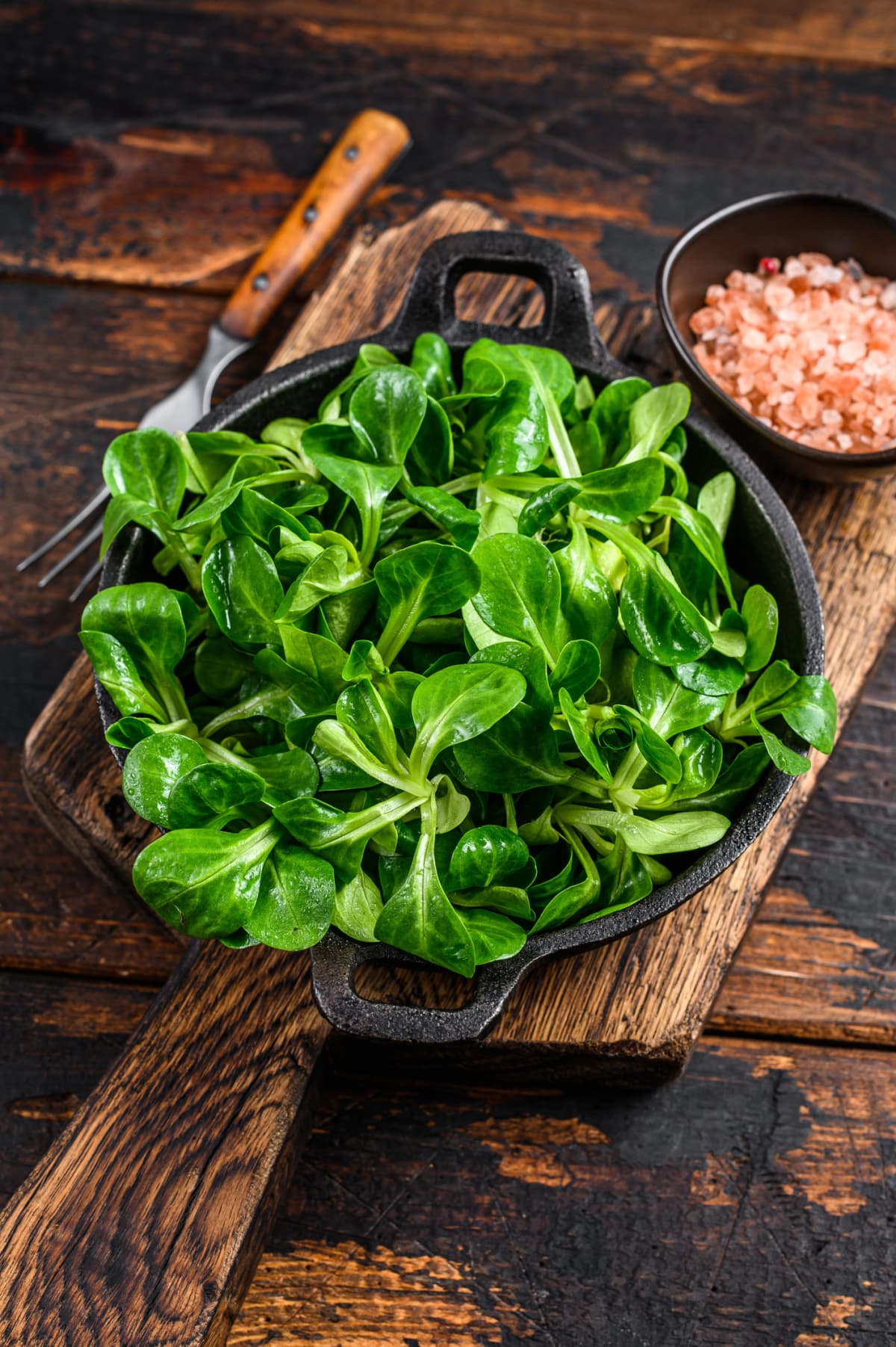 Fresh Raw green lambs lettuce Corn salad leaves in a pan. Dark wooden background. Top view.