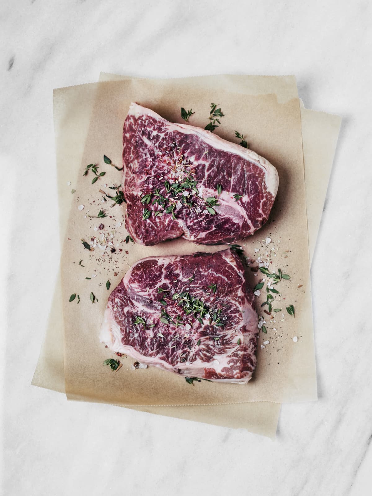 Two raw steaks with herbs on parchment paper
