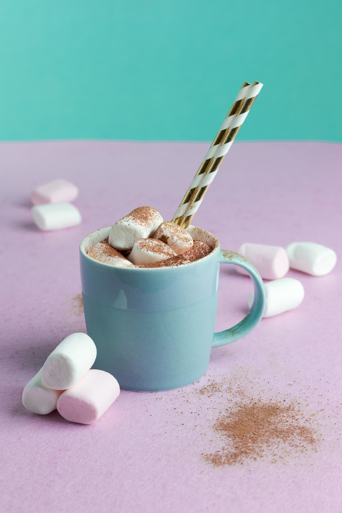 Vertical image of a cup of hot chocolate with stacked marshmallows and cacao, bright pastels pink turquoise copy space