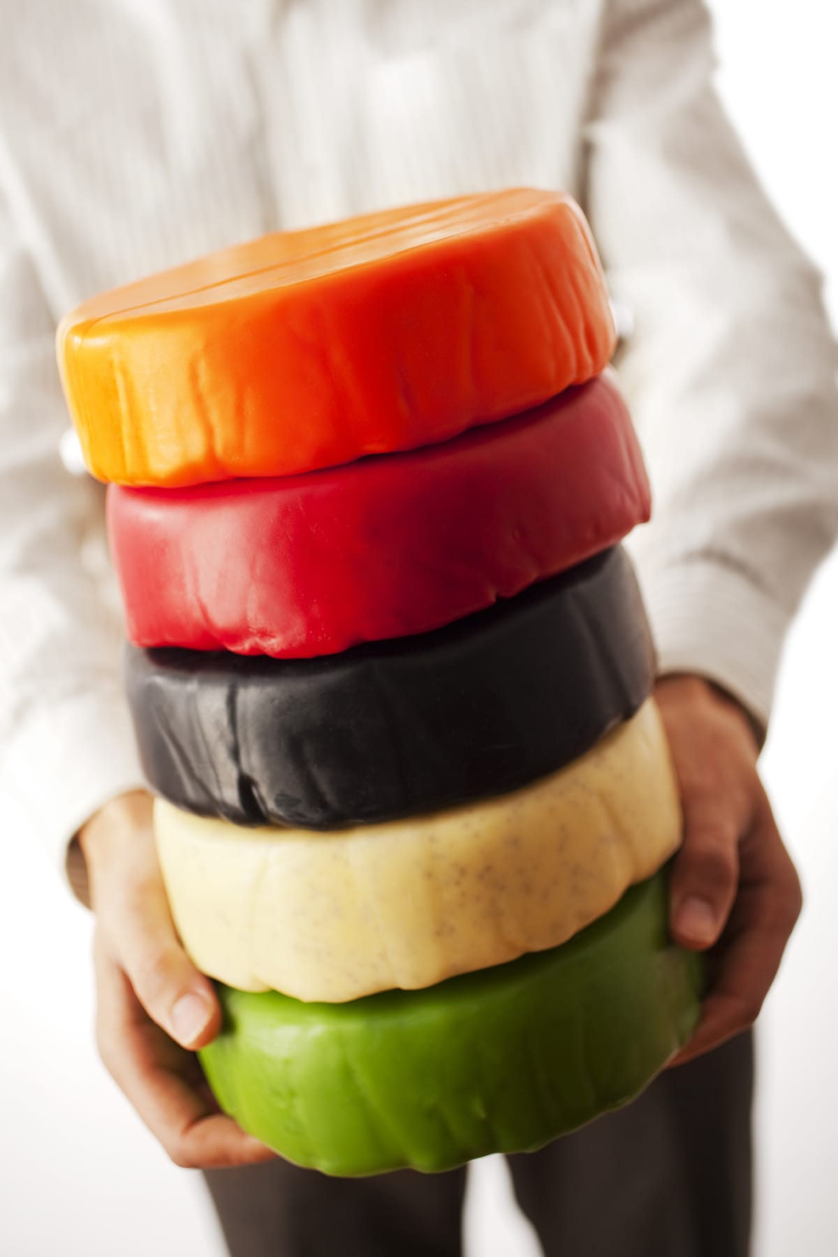 Man holding a stack of waxed multicolour wheels of cheddar cheese, Newport, Wales, 2009
