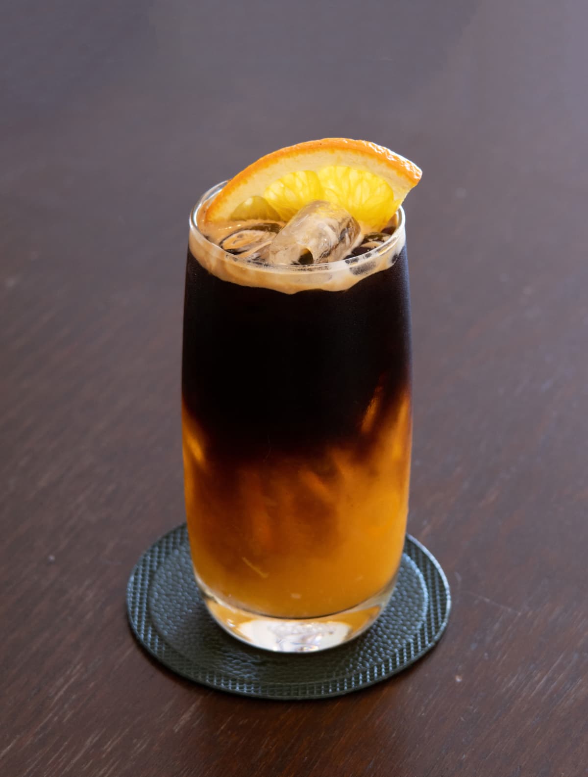 A glass of iced americano black coffee and layer of orange on wood table