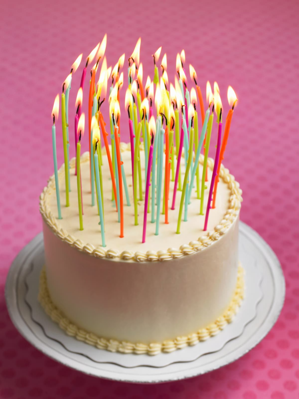 A birthday cake with many candles on a pink background
