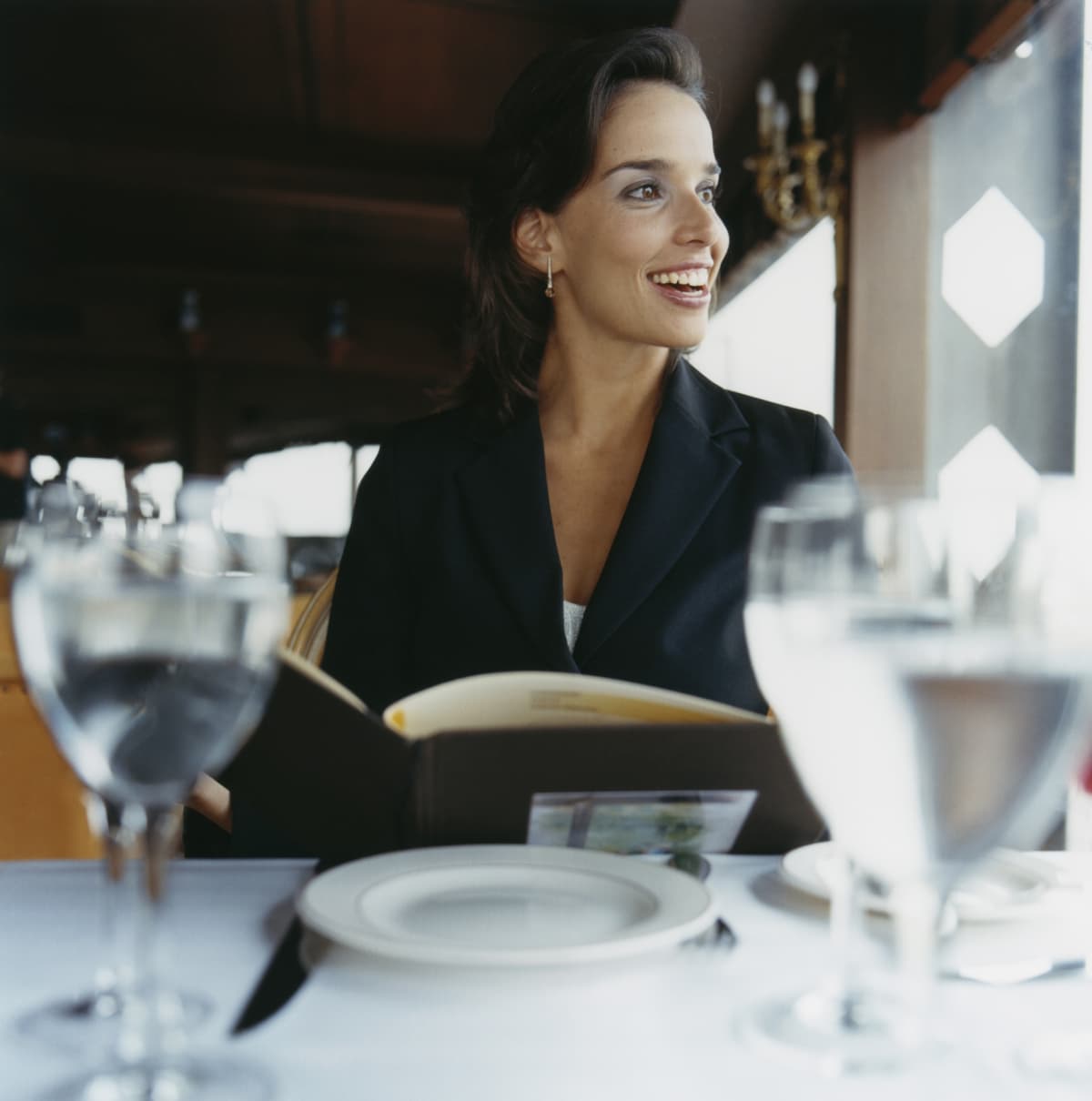 Young African American lady sitting in restaurant with cup of coffee in hand and thoughtfully looking at menu.Pretty girl in white shirt drinking coffee in cafe.Portrait of lady with dark curly hair