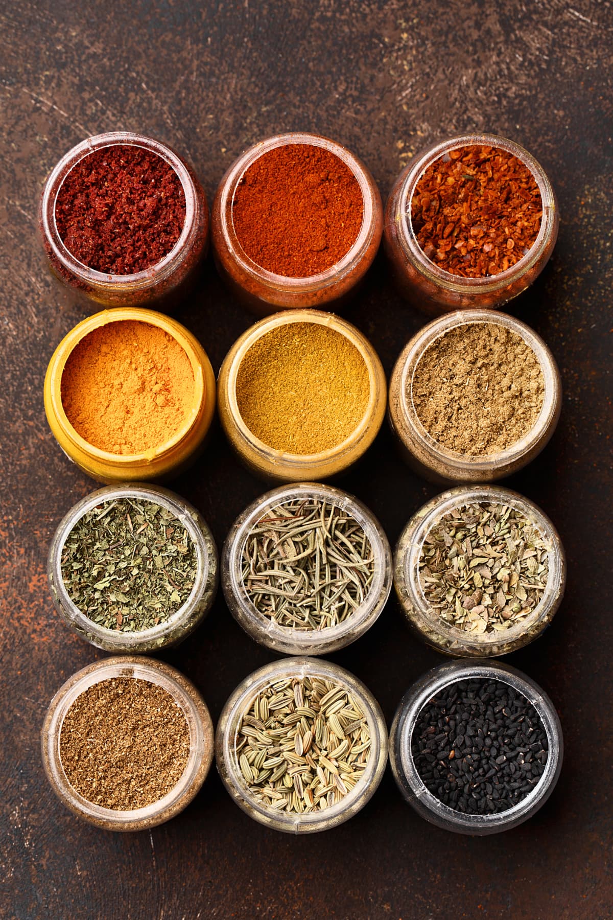 Set of various colorful spices in jars over dark brown concrete background. Top view, close up, flat lay. Food background, ingredients for cooking