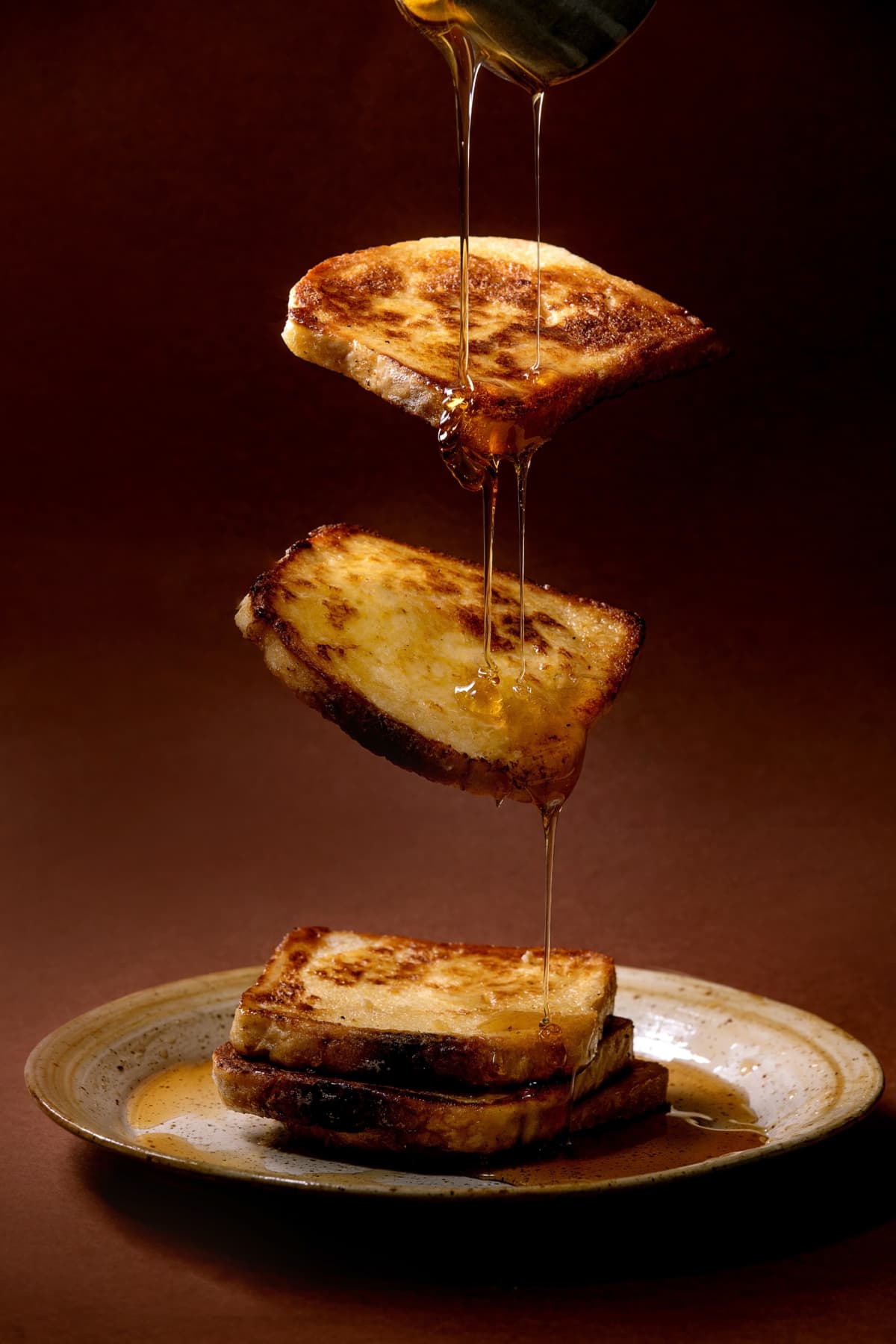 Flying french toasts on spotted ceramic plate with powring dripping maple syrup over brown texture background