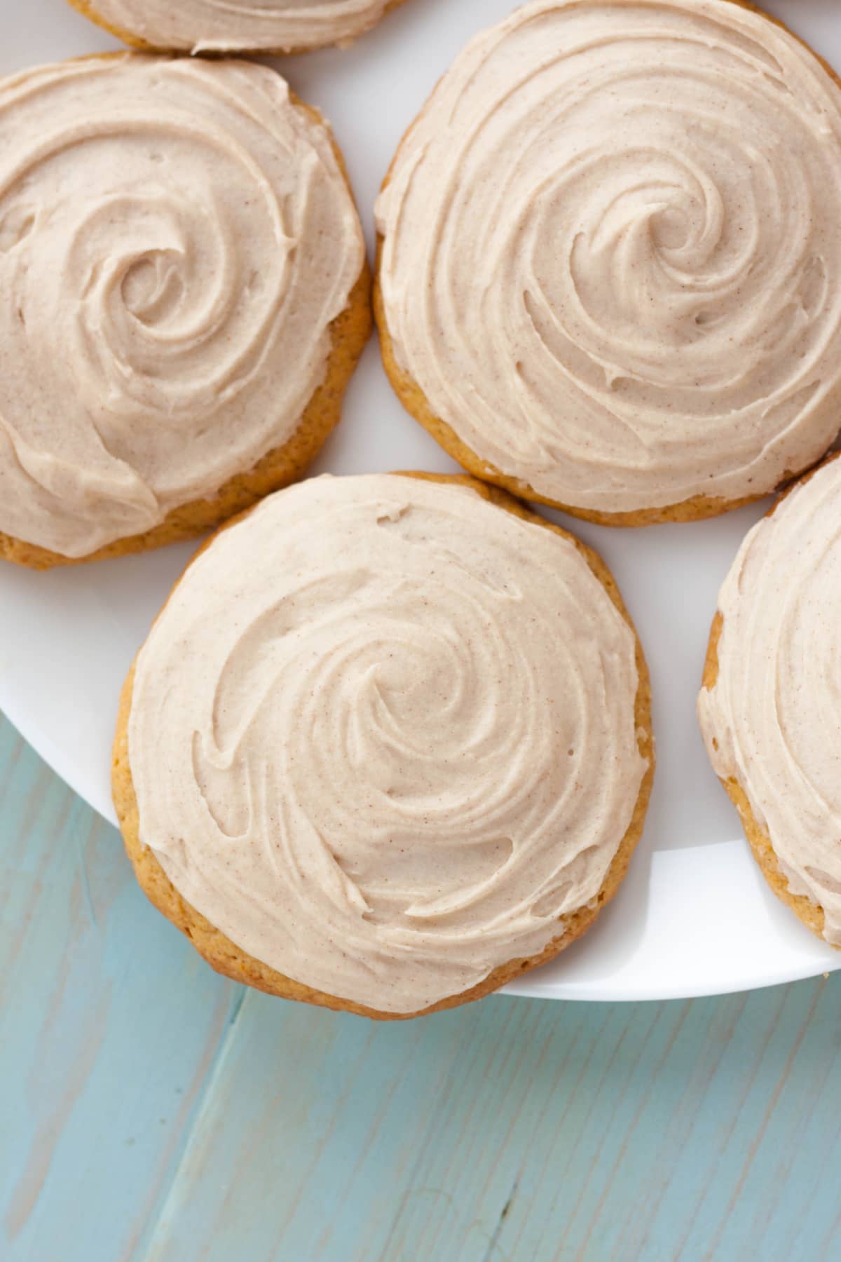 Round pumpkin cookies with cream cheese frosting on a white plate