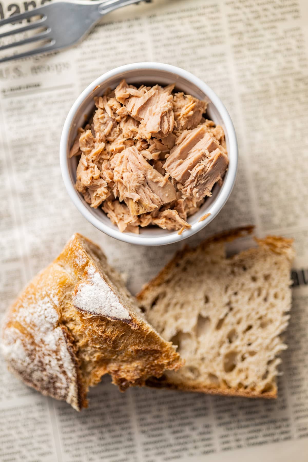 Canned tuna fish in a white bowl with pieces of bread below and a fork above