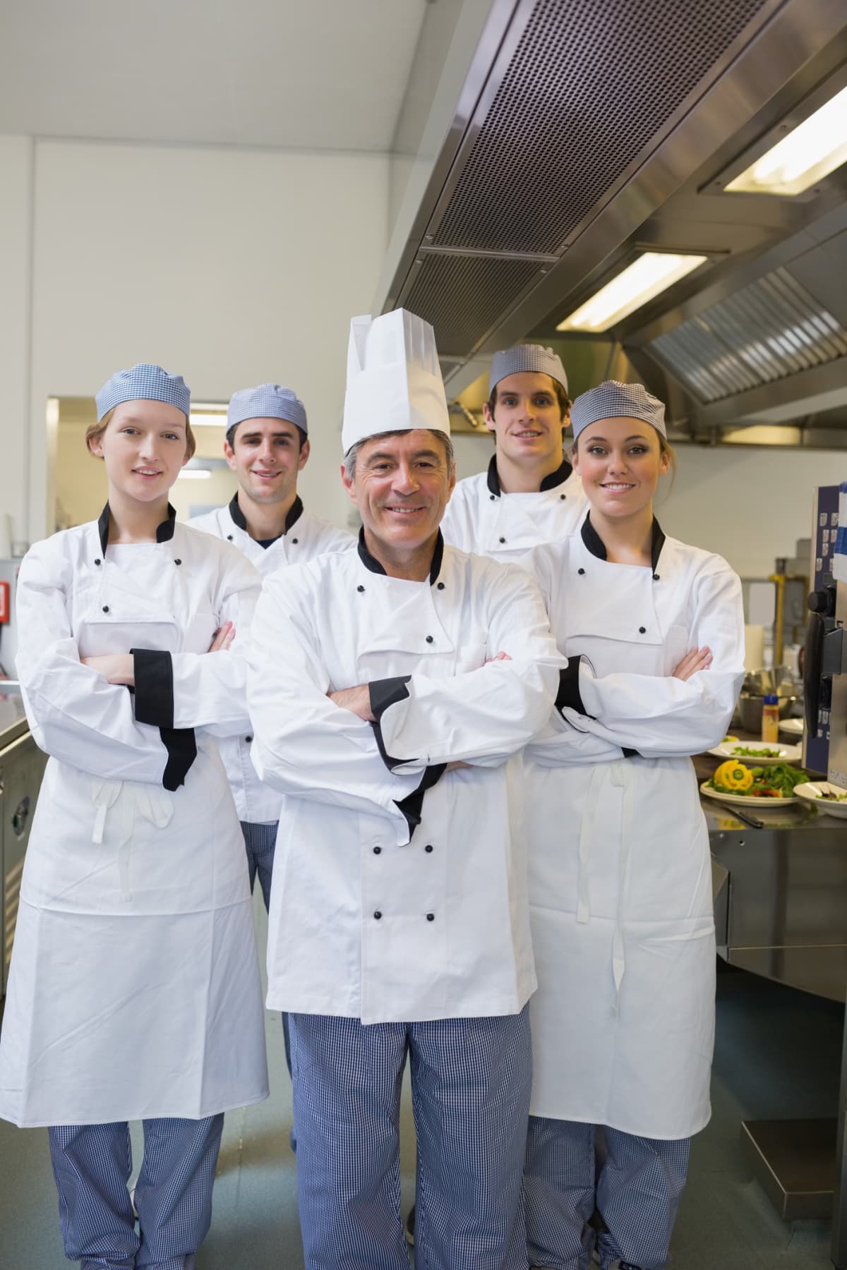 Smiling team of chefs standing with arms crossed in kitchen