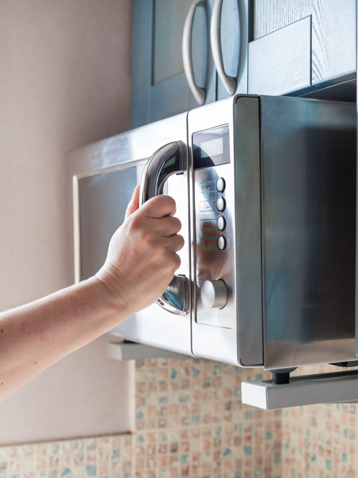 A person's hand gripping the door handle of a microwave