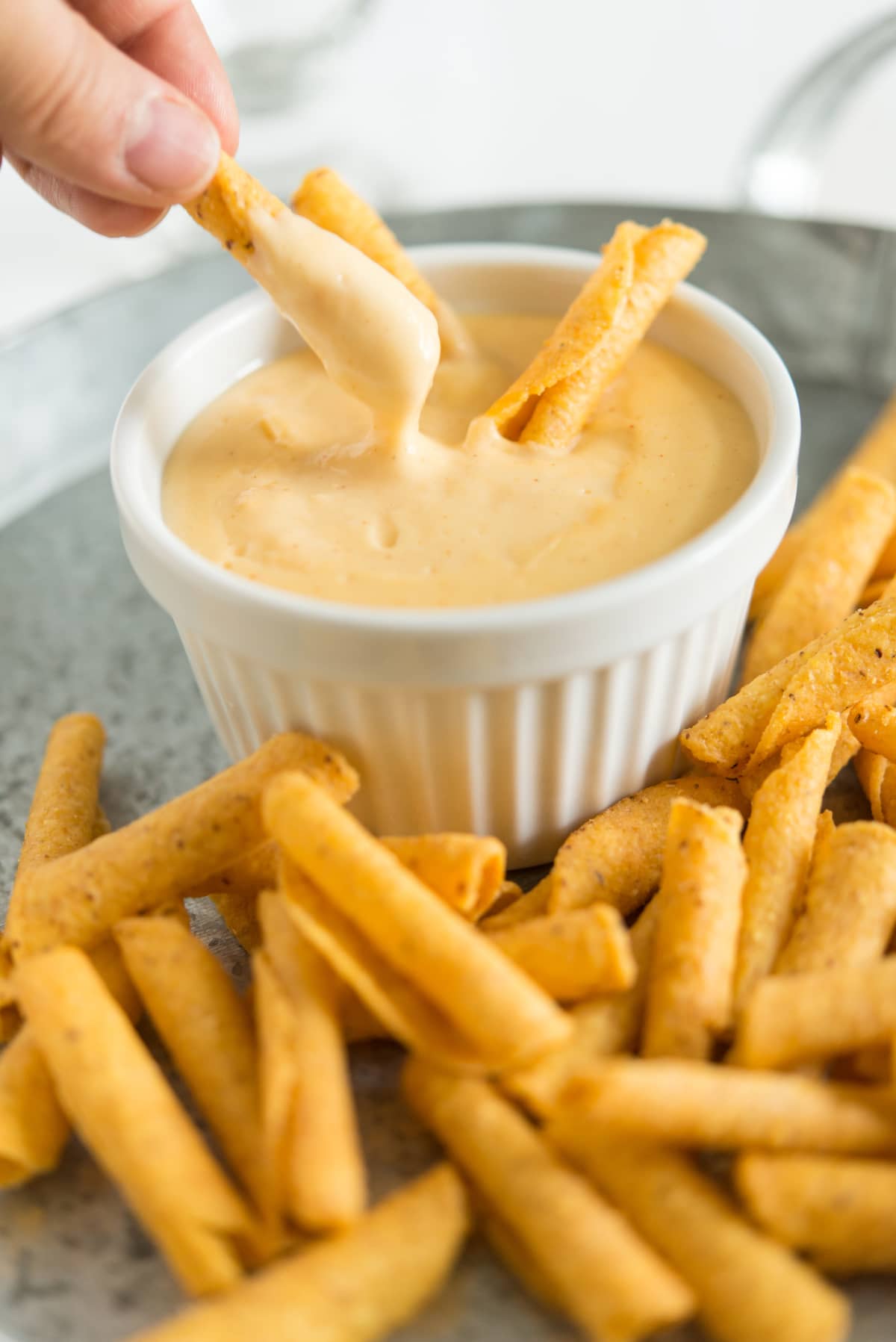 A person dipping a french fry in cheese sauce and fries around the sauce cup