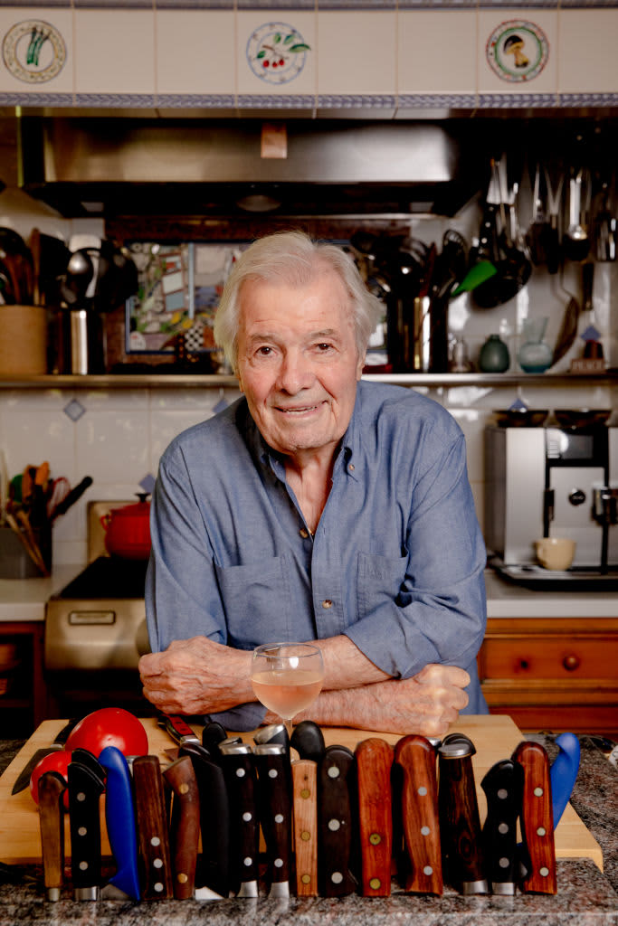 Chef Jacques Pepin smiling in a kitchen with his elbows resting on the counter