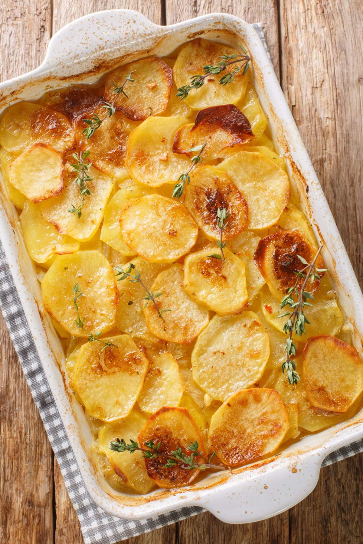 Baking tray of potatoes au gratin topped with fresh thyme sprigs