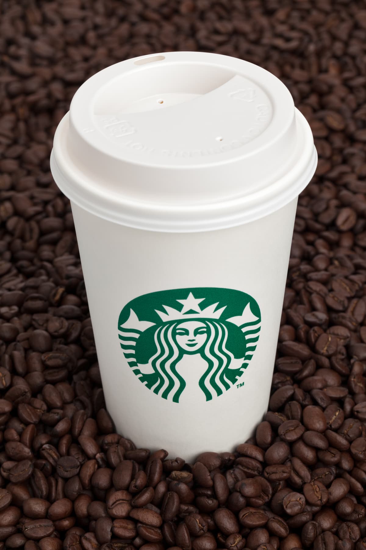 A white starbucks cup surrounded by arabica coffee beans