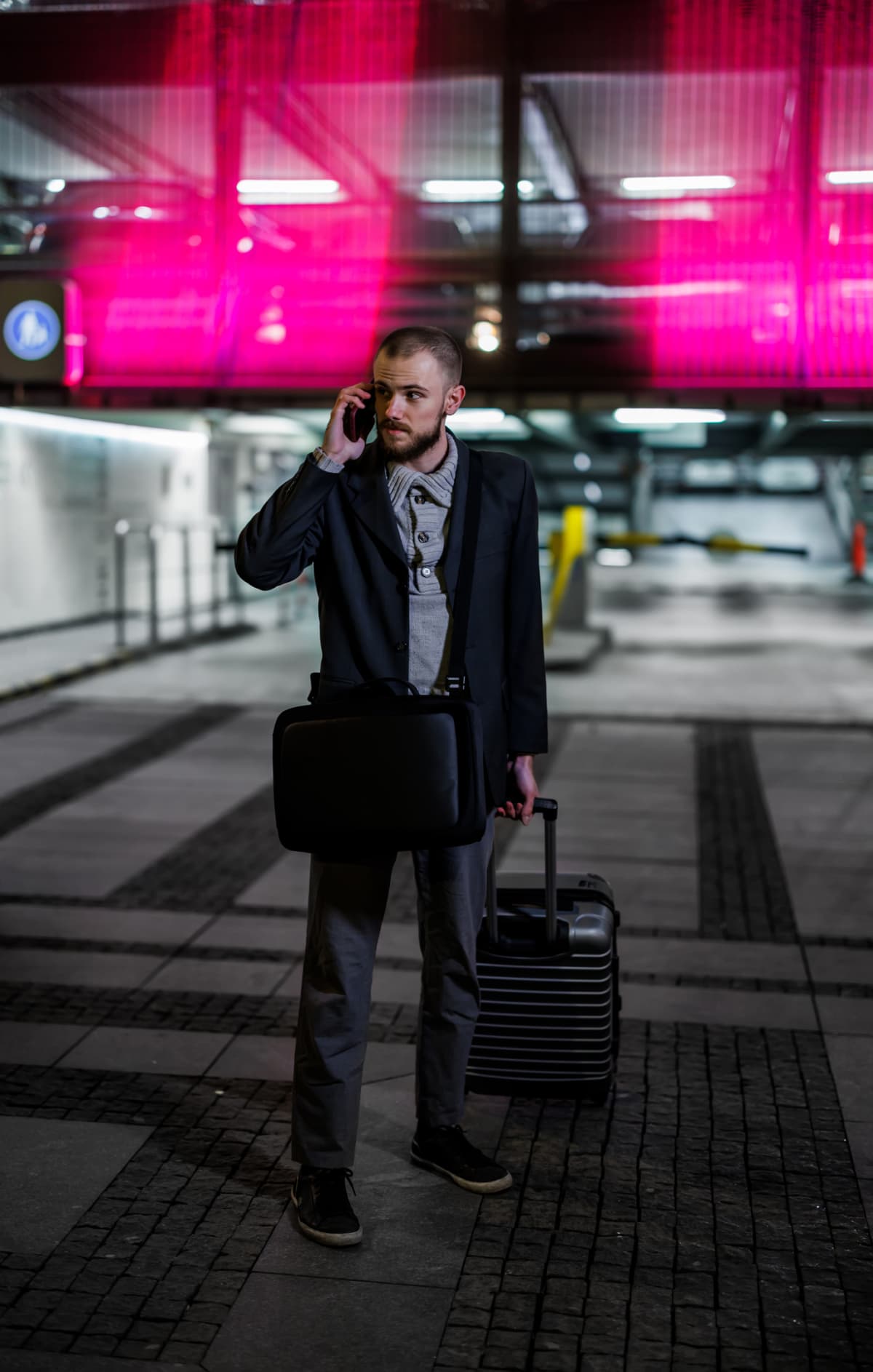 As a young businessman exits the airport with a suitcase, he is talking on a mobile phone.