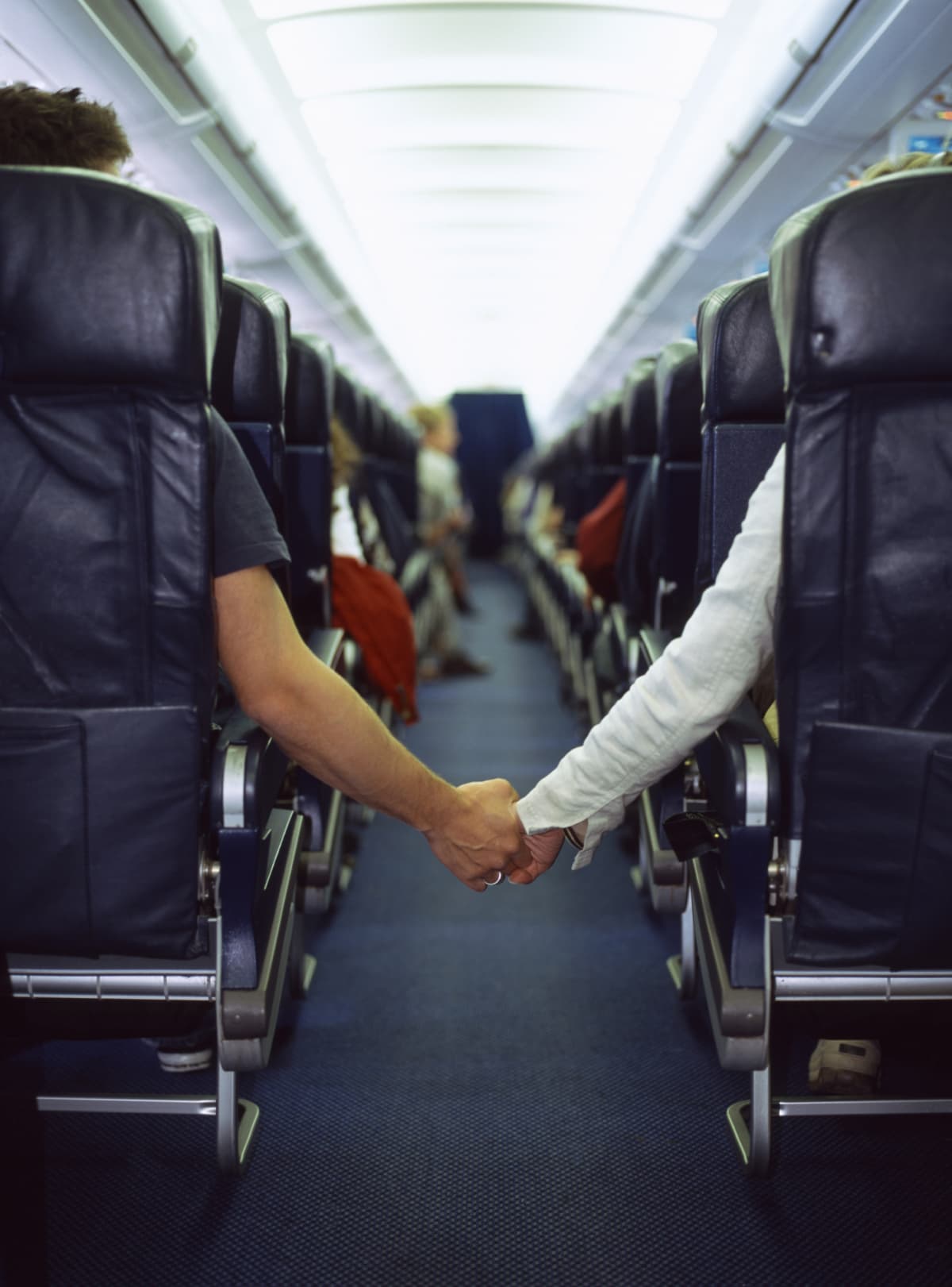 A man and woman hold hands across the airplane aisle