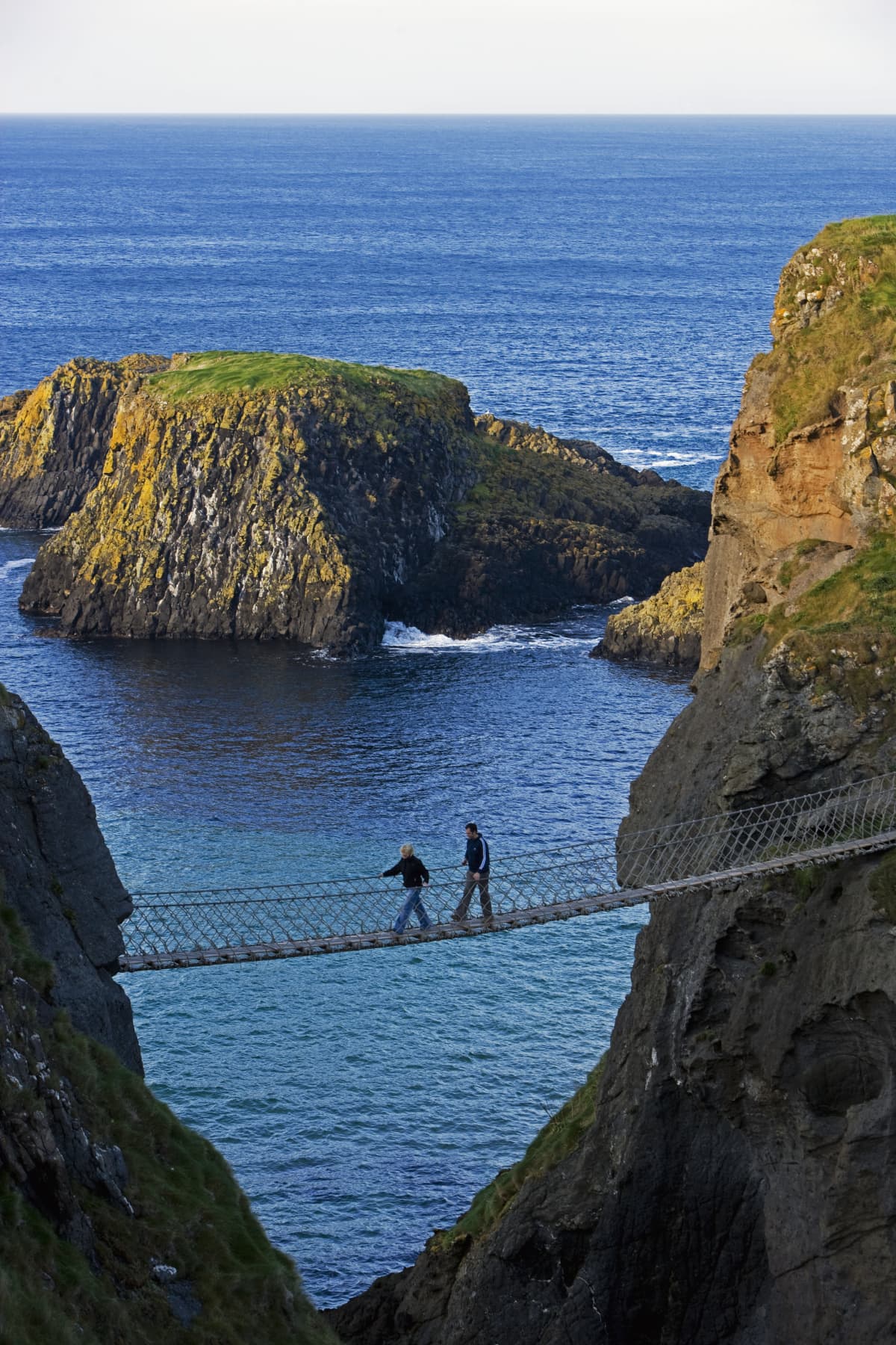 Two people walk on the rope bridge in Carrick-A-Rede