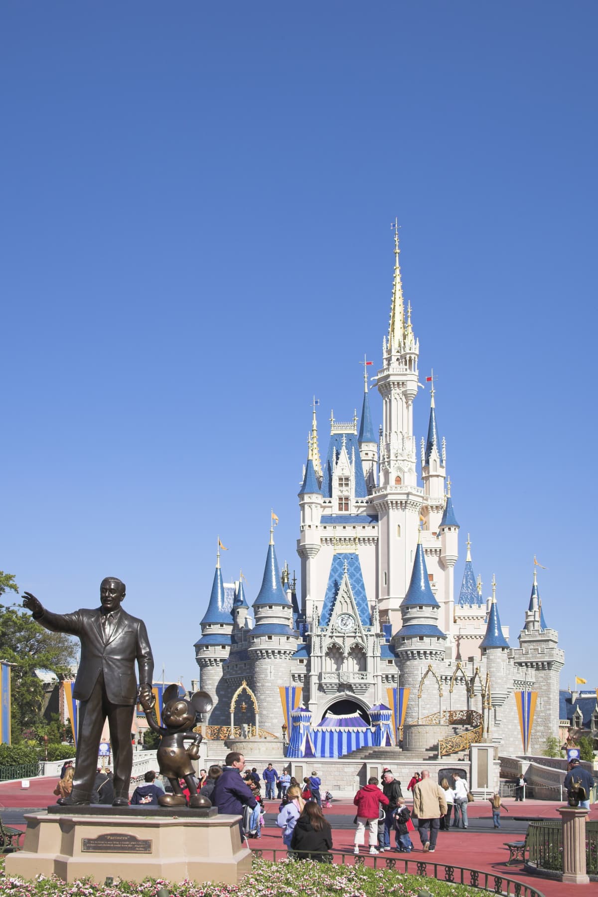 Tourists walk between the Walt Disney and Mickey Mouse statue and Cinderella's Castle at Disney World.