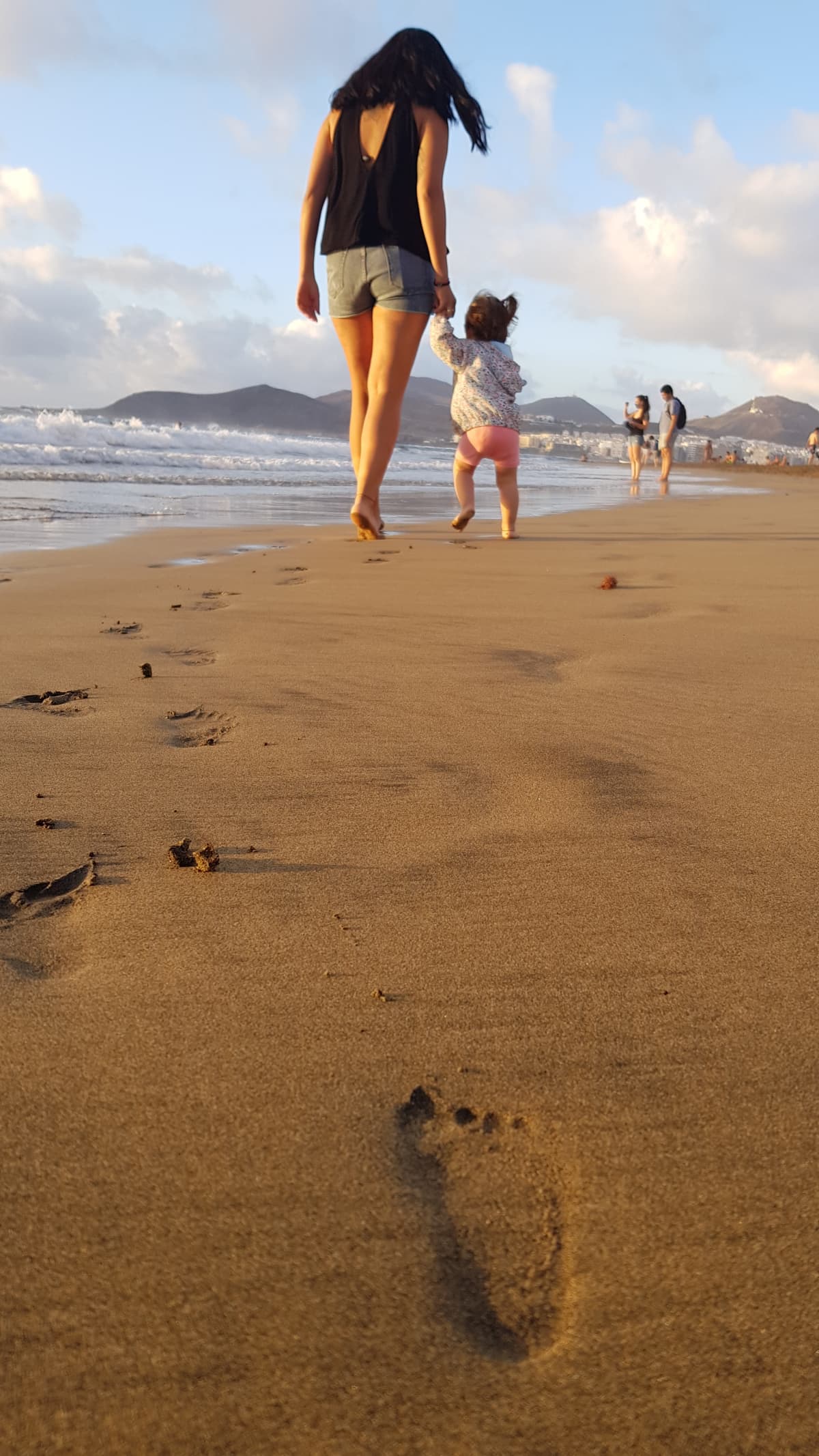 A mother and daughter walking in the sand at the beach