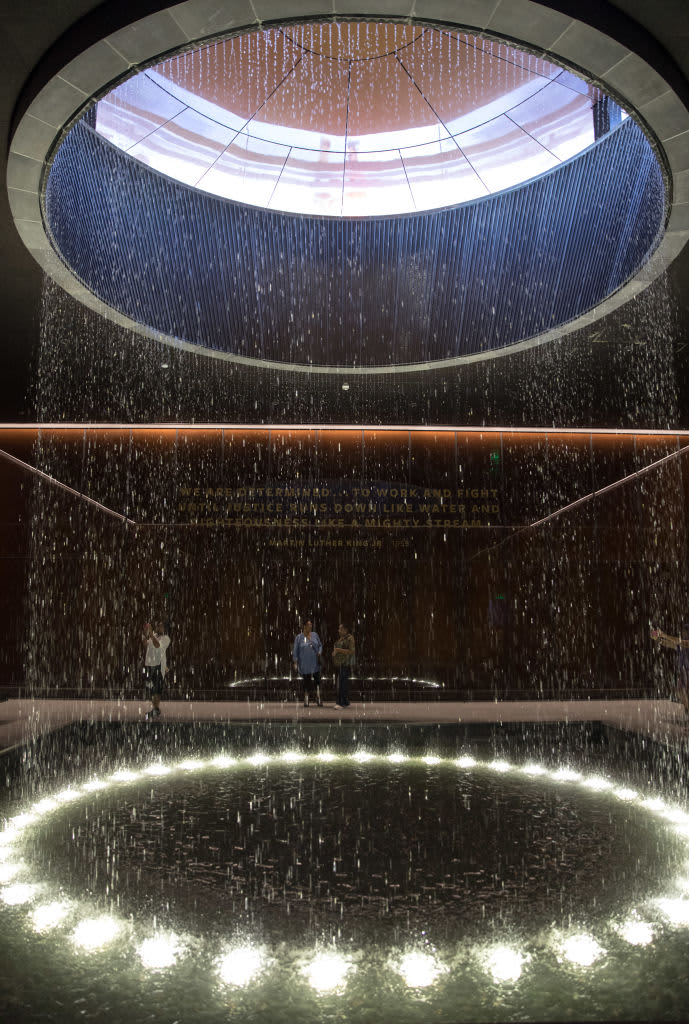 WASHINGTON, DC-SEP7: Visitors to the Contemplative Court at the National Museum of African American History and Culture, September 7, 2017, in Washington, DC. Now that the reflective space is open, and has become a favorite spot in the museum, it stands for both the strengths and weaknesses of the museums larger form, created by lead designer David Adjaye and lead architect Philip Freelon. The building is conceptually strong, but sometimes weak on details. The drama of light and water in the Contemplative Court is as beautiful and striking as the basic design of the corona on the buildings exterior, but there is already corrosion on the ceiling panels near where the water is released. On a recent visit, it also seemed strange that, to enter the room, one had to walk up a ramp because the court is slightly higher than museums underground concourse. This only adds to the jumble of elevations throughout the history galleries, which are accessed by an elevator from the first underground level, which is in turn accessed by another elevator or stairway from ground level. (Photo by Evelyn Hockstein/For The Washington Post via Getty Images)