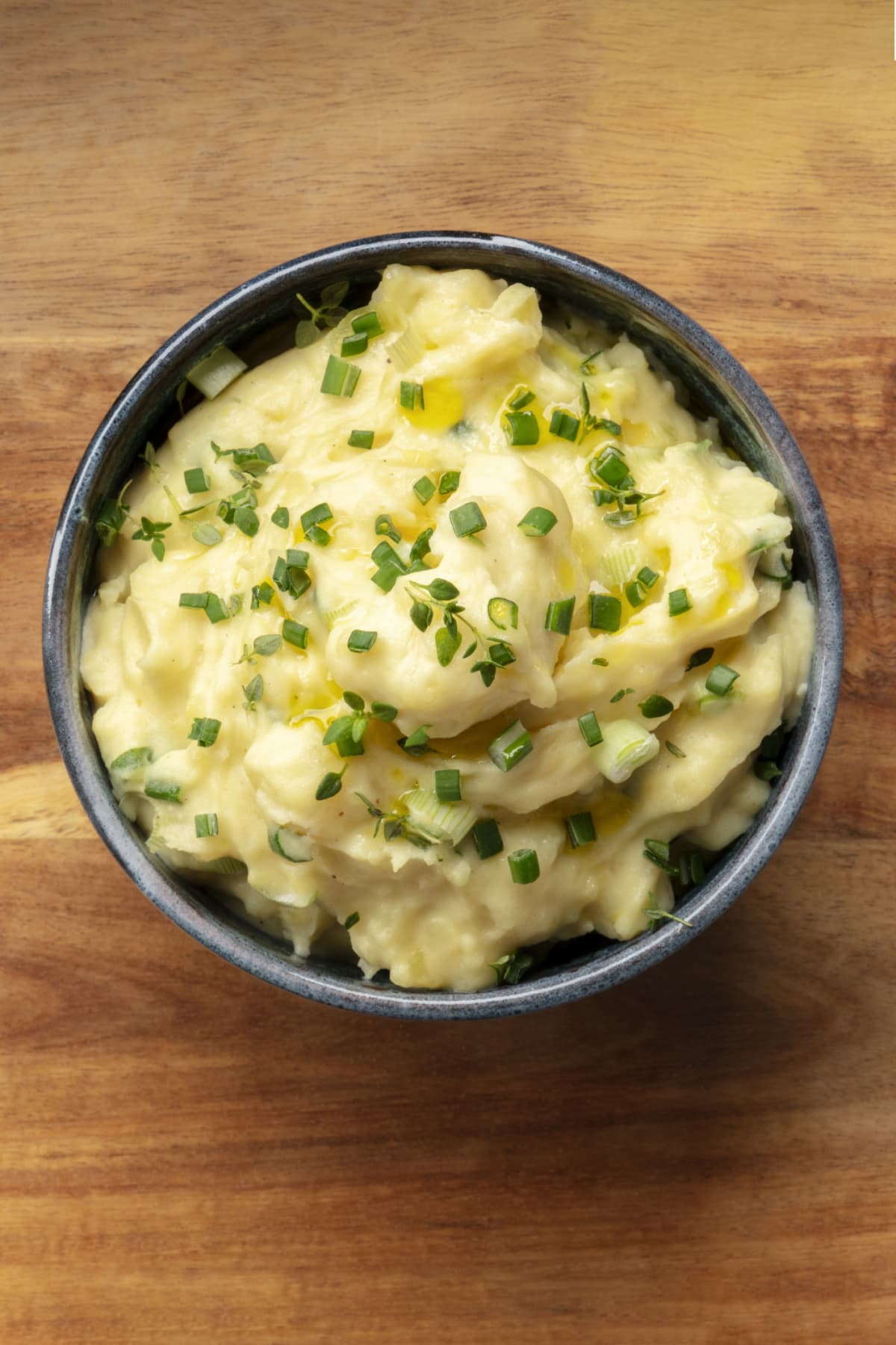Pomme puree, an overhead photo of a bowl of potato puree with herbs, shot from the top on a rustic background with a place for text