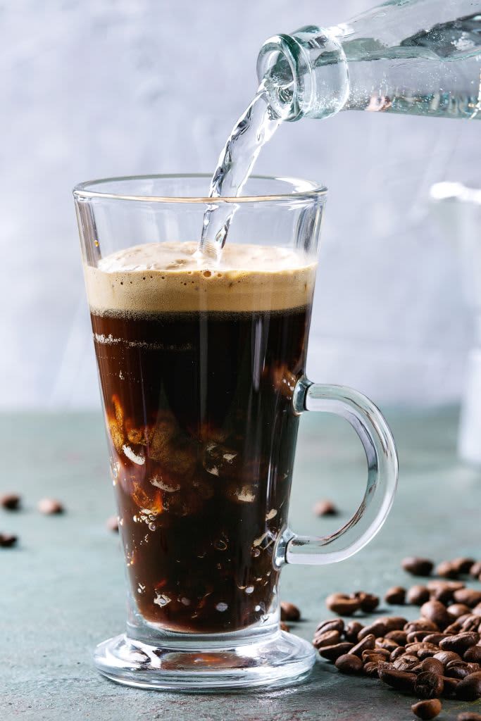 Fizzy iced Coffee espresso with pouring sparkling water from bottle and roasted beans around over grey green texture table Modern drink. (Photo by: Natasha Breen/REDA&CO/Universal Images Group via Getty Images)