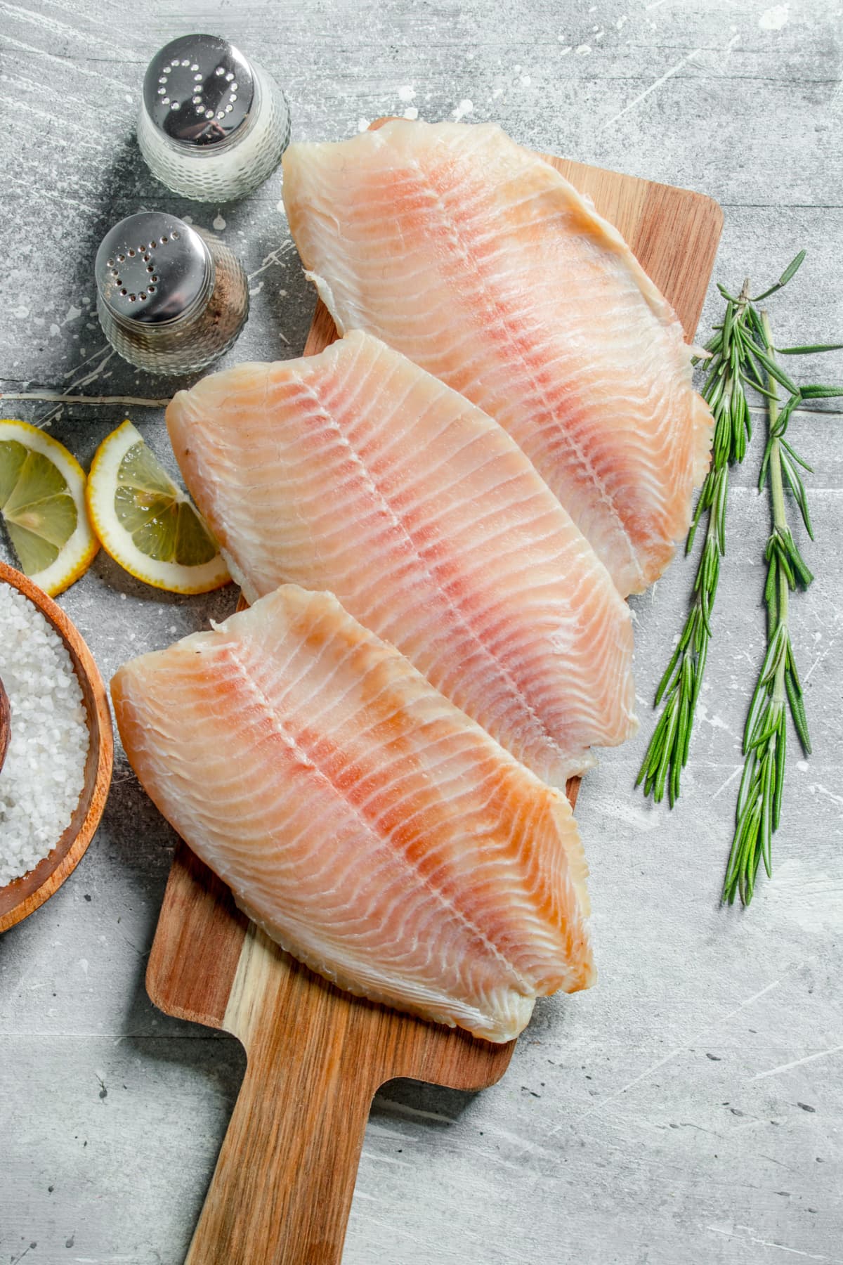 Fish fillet on a wooden cutting Board with rosemary, spices and lemon slices. On white rustic background
