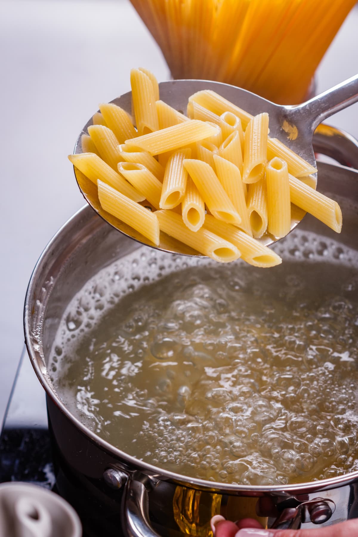 Penne pasta held in a large silver spoon over a pot of boiling water