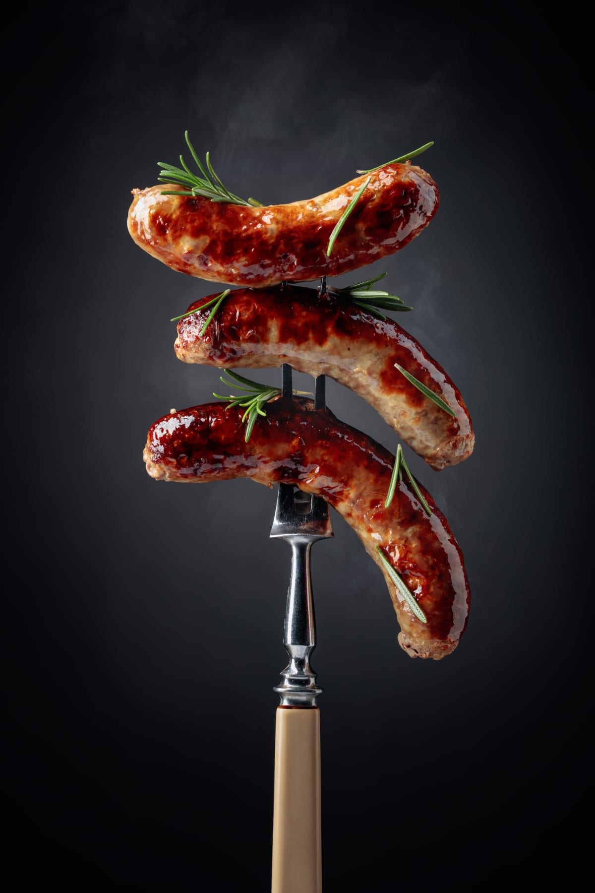 Grilled Bavarian sausages with rosemary on a fork on dark background