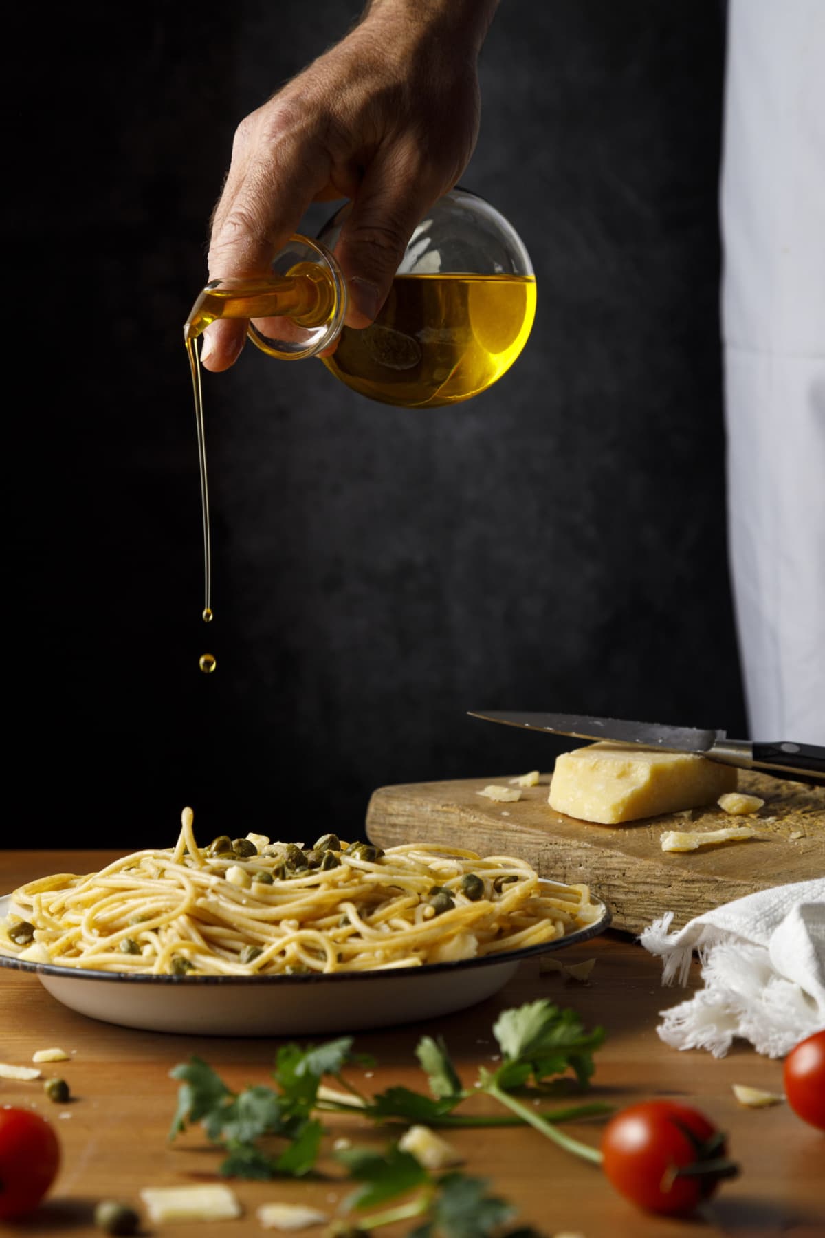 Man pouring olive oil on spaghetti on a plate
