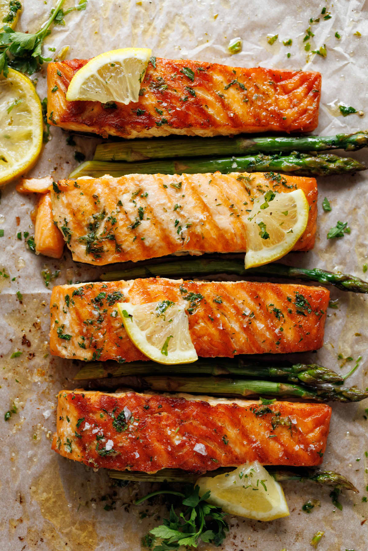 Grilled portions of salmon and green asparagus with lemon slices and herbs, top view