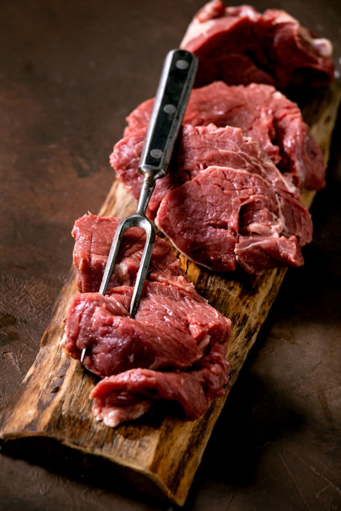 Sliced raw beef tenderloin meat for steaks on wooden board with metal meat fork. salt and pepper over dark brown texture background. Food cooking background concept. Close up. (Photo by: Natasha Breen/REDA&CO/Universal Images Group via Getty Images)