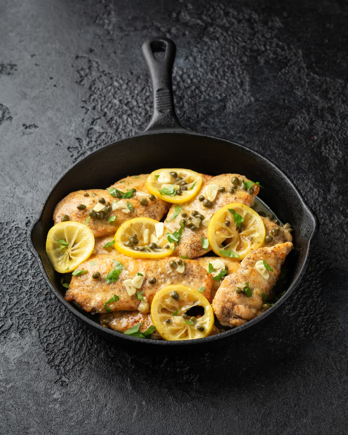 Cast iron skillet with chicken topped with capers, lemons, and herbs