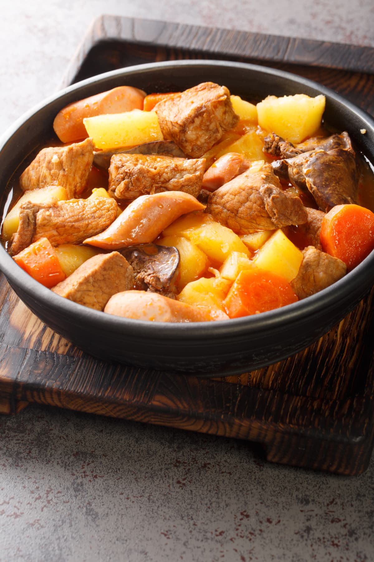 Pork Menudo is a Filipino pork stew dish with carrots and potato close up in the plate on the table. Vertical