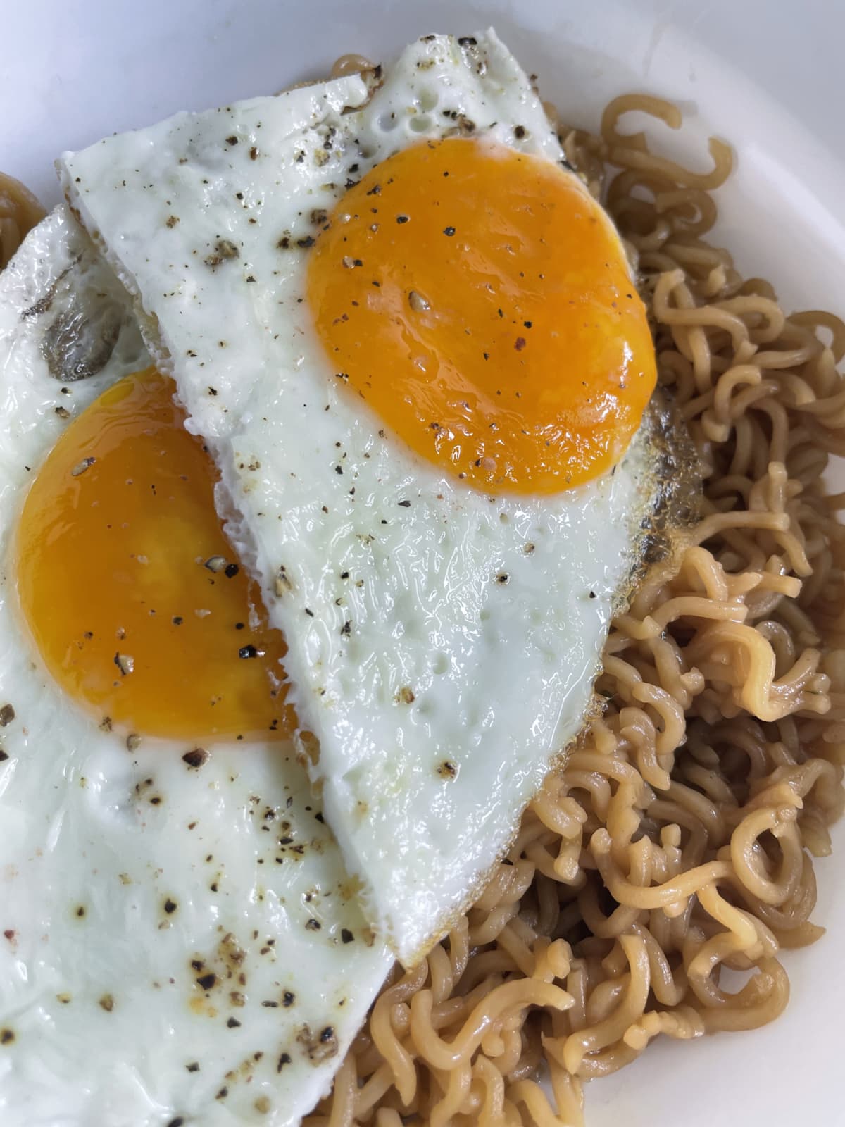 Stock photo showing elevated view of a plate containing a meal of sunny side up fried eggs seasoned with pepper served with noodles.