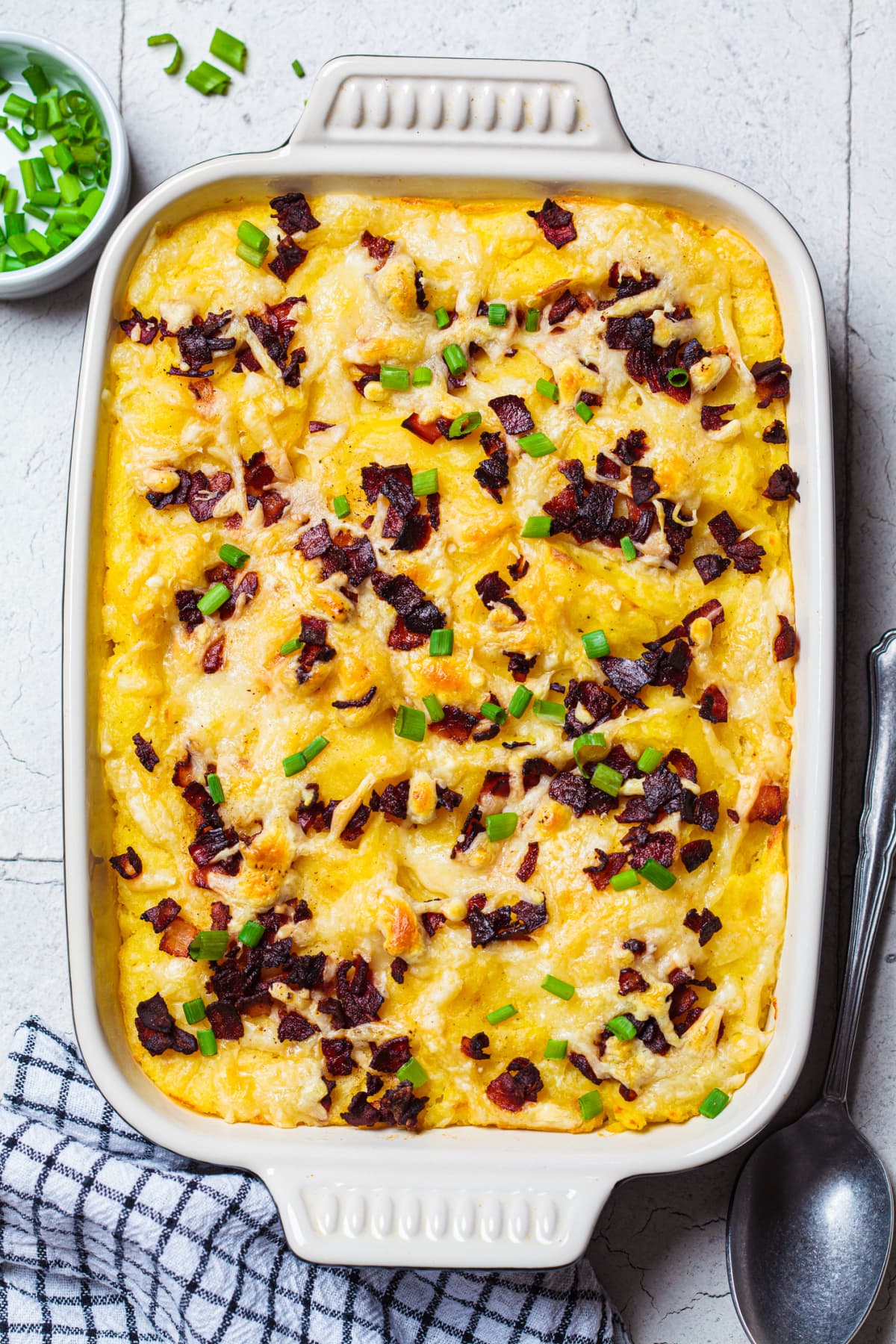 A casserole dish of mashed potatoes with cheese, bacon, and green onions