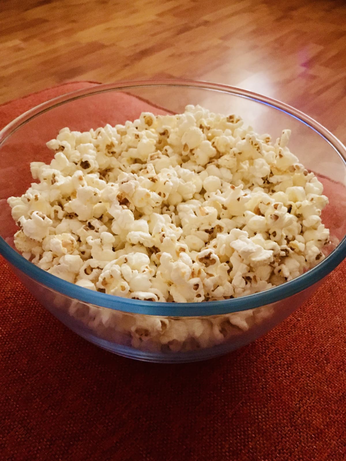 Freshly prepared popcorn in a glass bowl on a red surface
