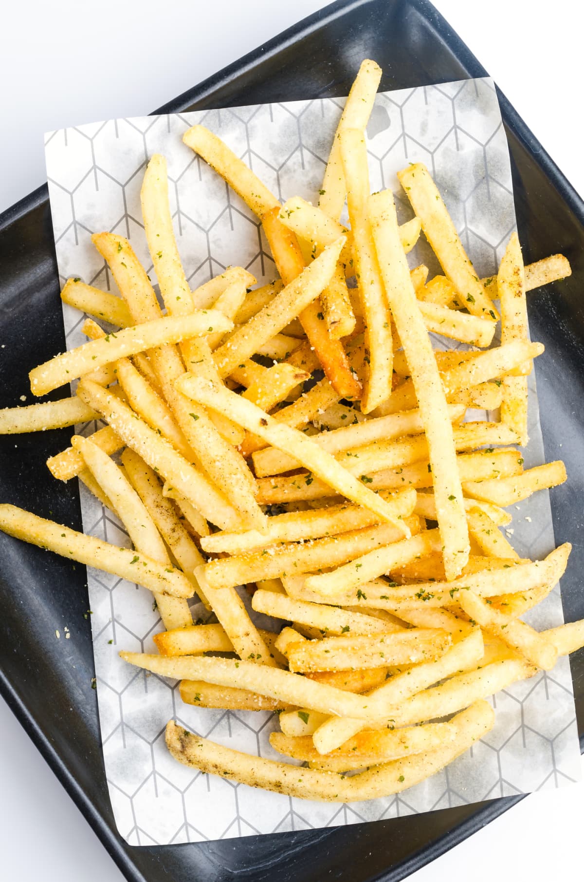 Seasoned french fries on a baking tray on a white background