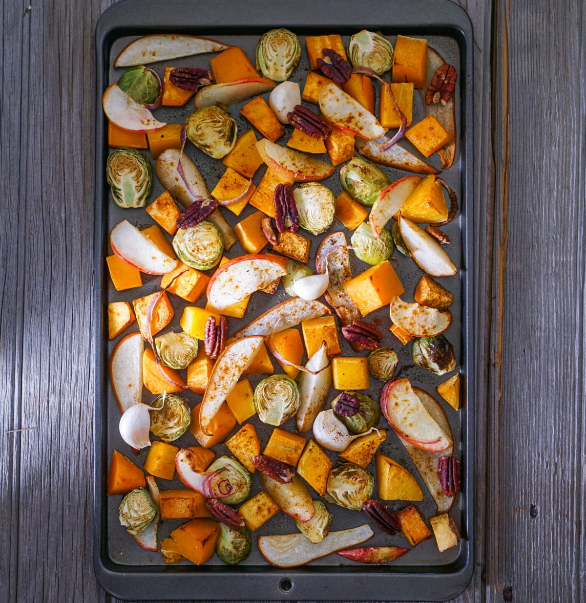 Roasted root vegetables on a baking sheet: sweet potato, butternut squash, brussels sprouts, apple, pecans and pear. Toning. Healthy eating concept.