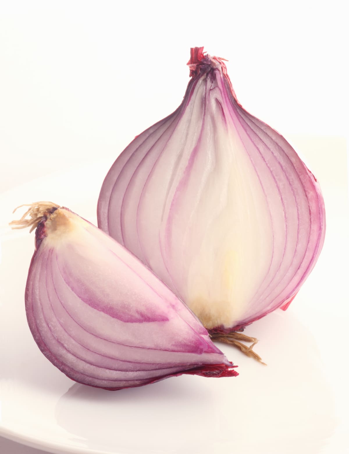 Half a red onion showing layers inside, with a quarter of an onion placed in front of it, on a white background