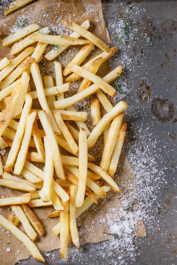 Fast food french fries potatoes with skin served with salt and herbs on baking paper over old rusty metal background. Top view, space for text. (Photo by: Natasha Breen/REDA&CO/Universal Images Group via Getty Images)