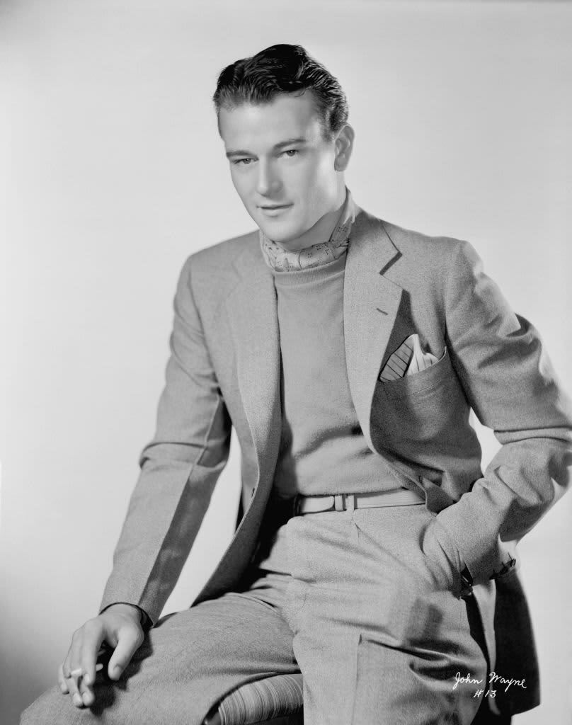 Black and white photo of a young John Wayne seated