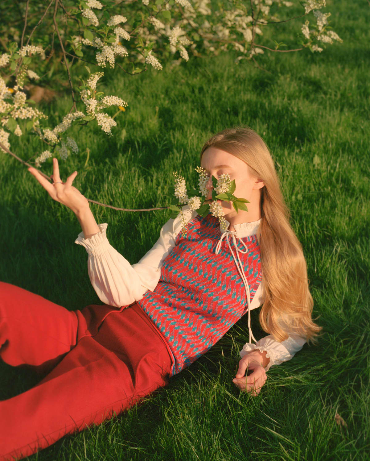 Woman laying in the grass and holding a flower up to her face