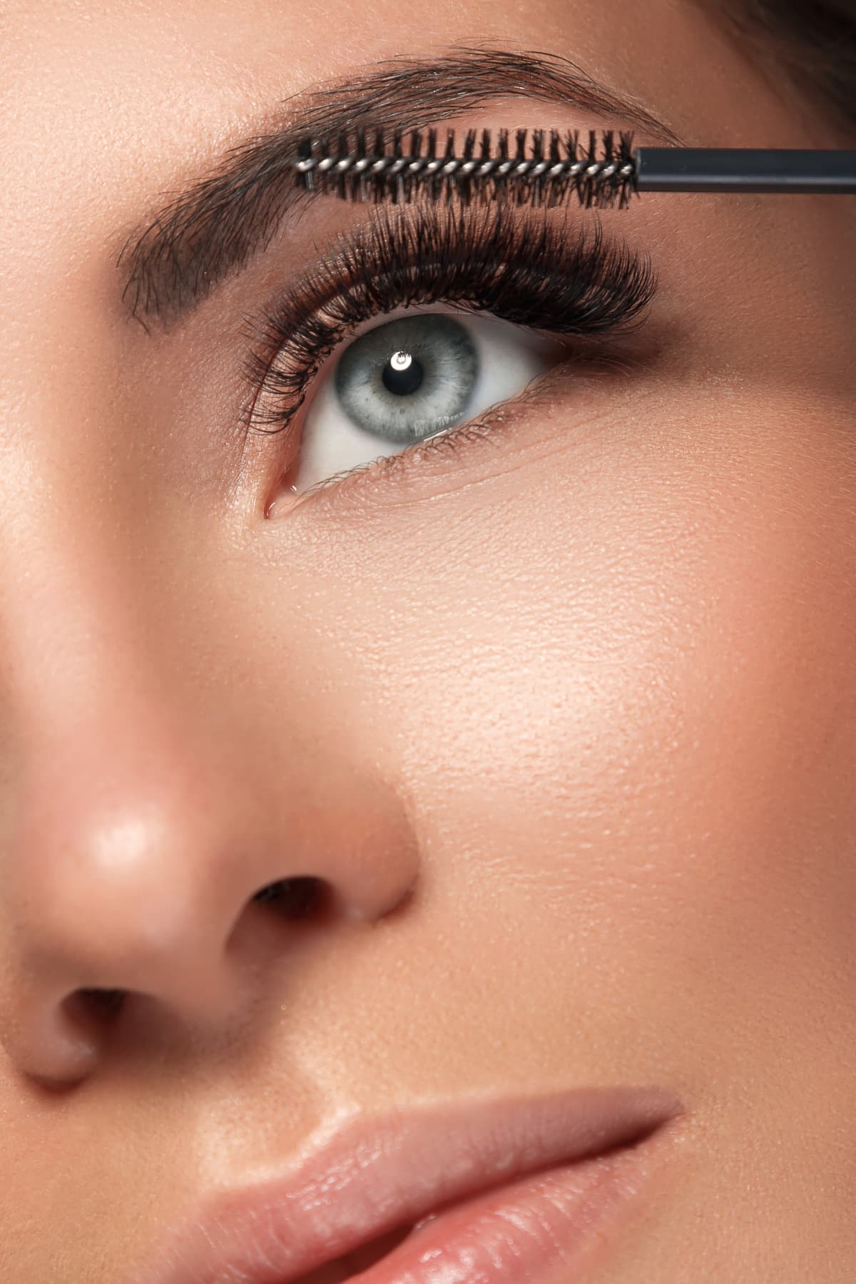Close up of a woman using a mascara wand on her thick, luscious eyelashes