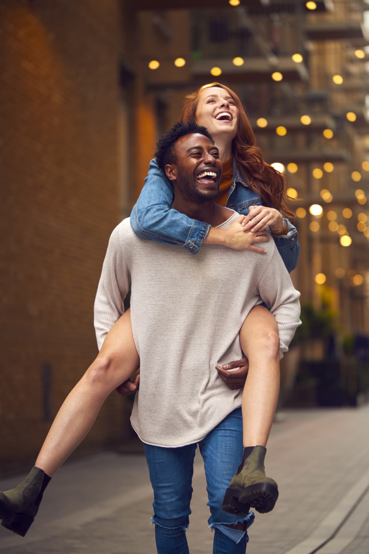 Portrait Of Young Couple Enjoying City Life Heading For Night Out With Man Giving Woman Piggyback