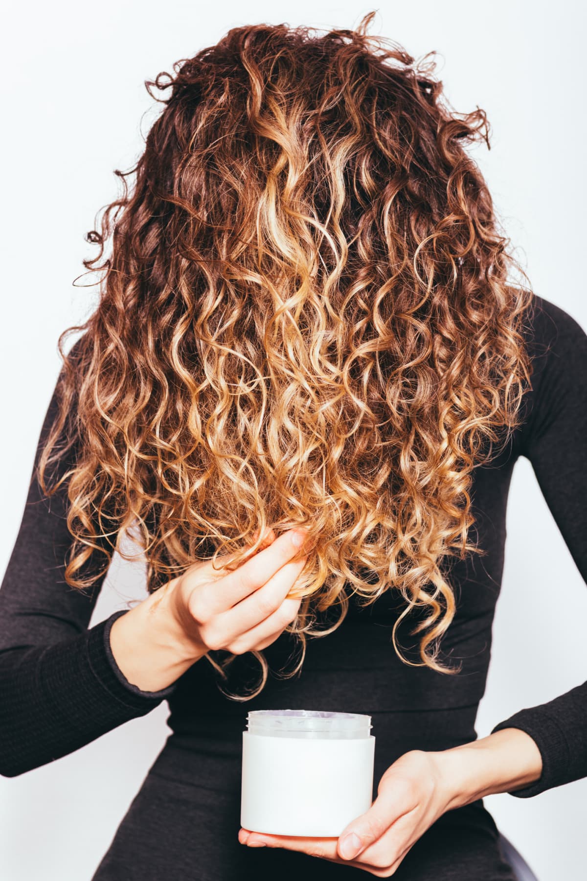 Woman applying moisturizing oil to her long curly hair