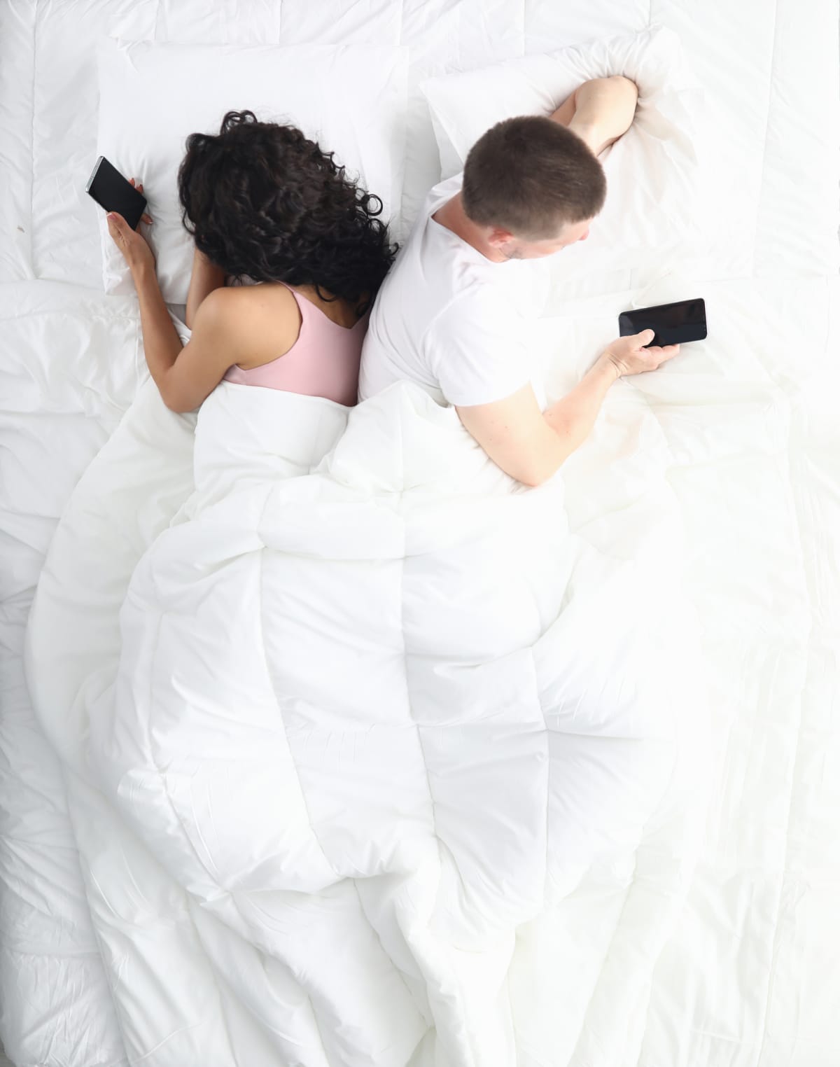 A couple in bed laying back to back on their phones