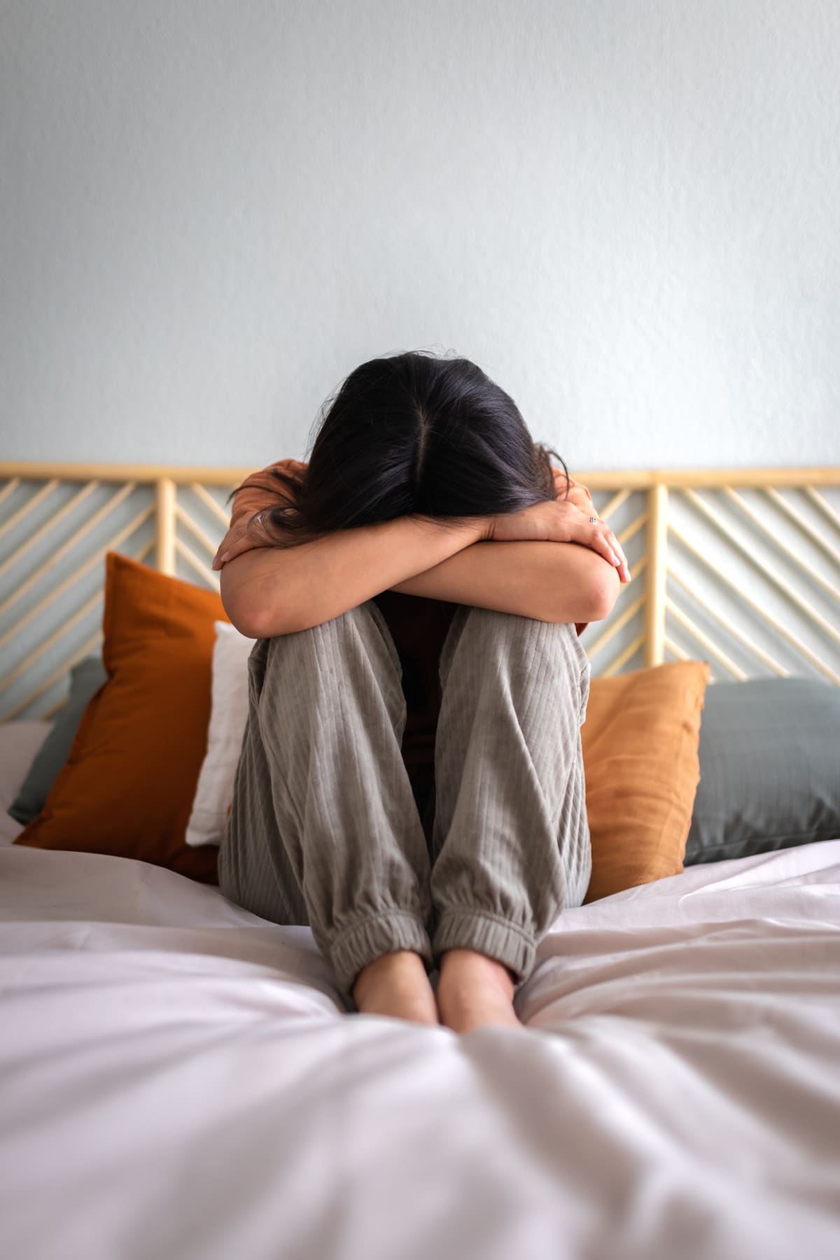 Front view of depressed and sad young woman sitting on the bed crying. Vertical image. Sadness and mental health concepts.