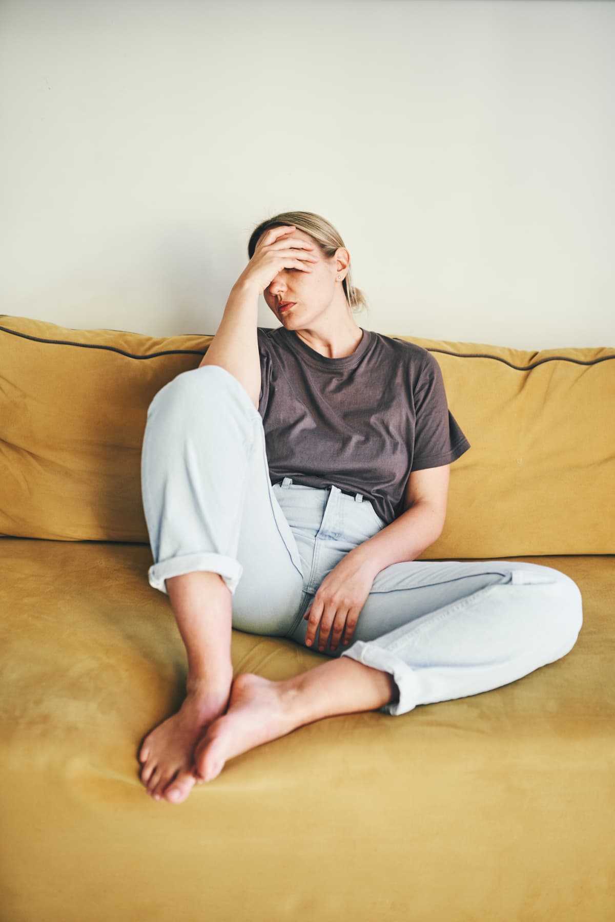 Woman looks frustrated as she sits on a couch with her head in her hand