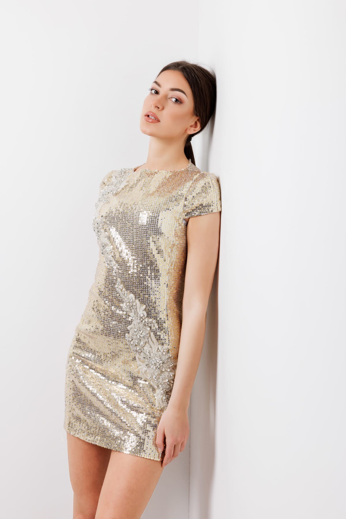 Woman in a champagne-colored sparkly dress leaning against a wall