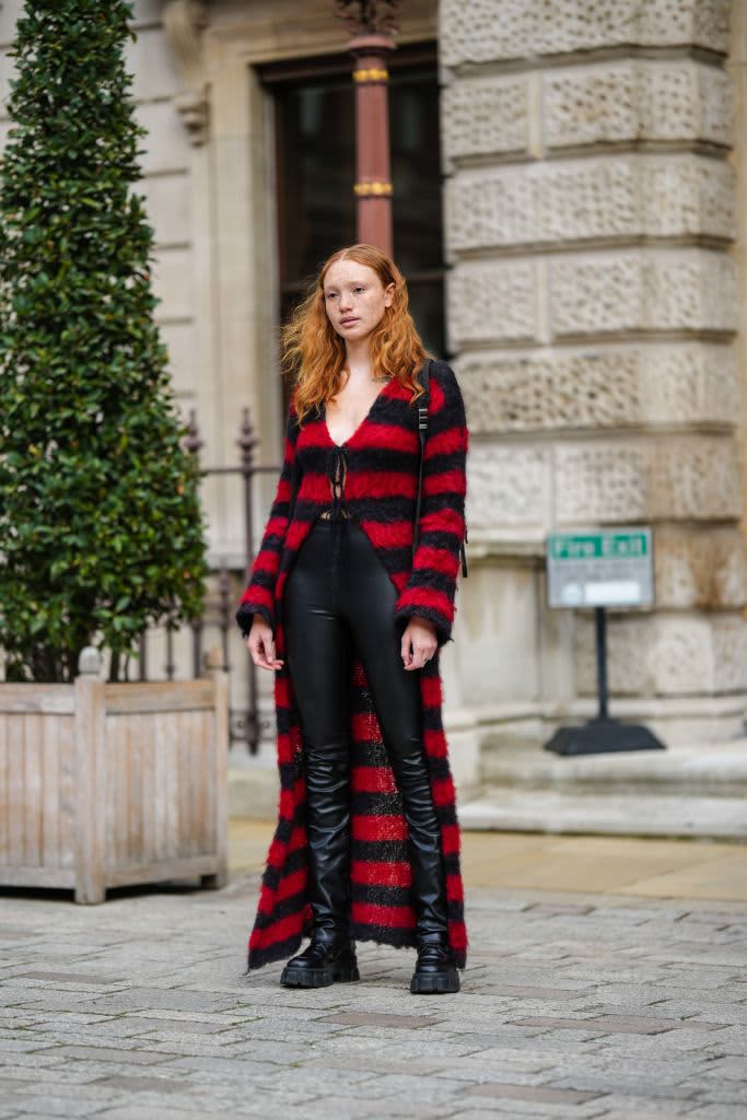 LONDON, ENGLAND - FEBRUARY 20: A model wears a red and black striped print pattern wool buttoned long cardigan black shiny leather skinny pants, a black back pack bag, black shiny leather ankle boots , outside Emilia Wickstead, during London Fashion Week February 2023 on February 20, 2023 in London, England. (Photo by Edward Berthelot/Getty Images)